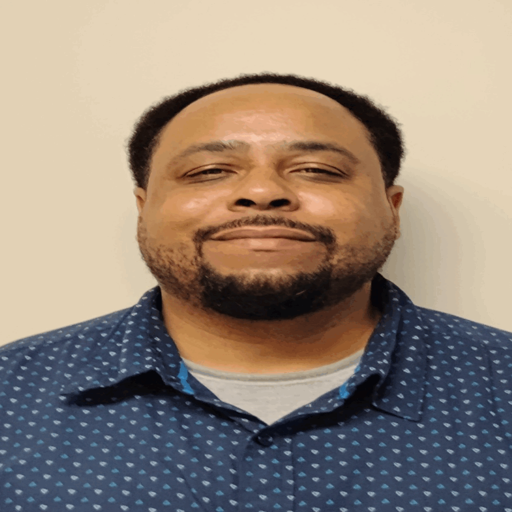 Smiling man in a blue patterned shirt.